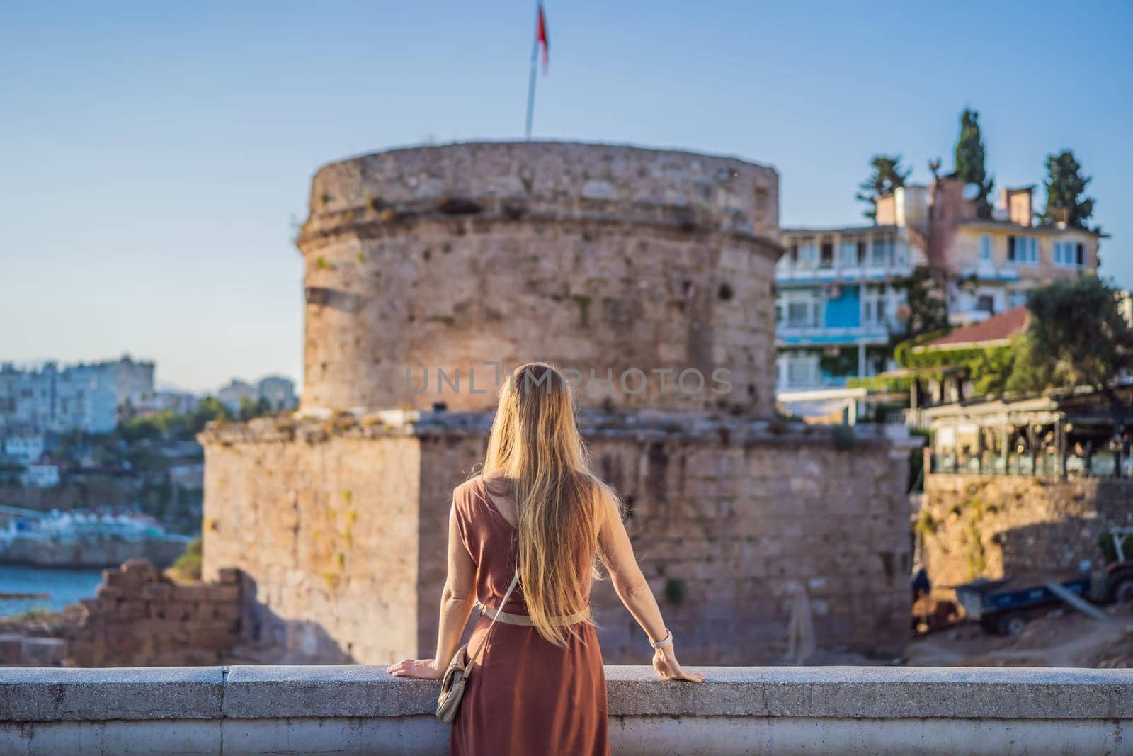 Woman tourist on background of Hidirlik Tower in Antalya against the backdrop of the Mediterranean bay of the ancient Kaleici district, Turkey. Turkiye.