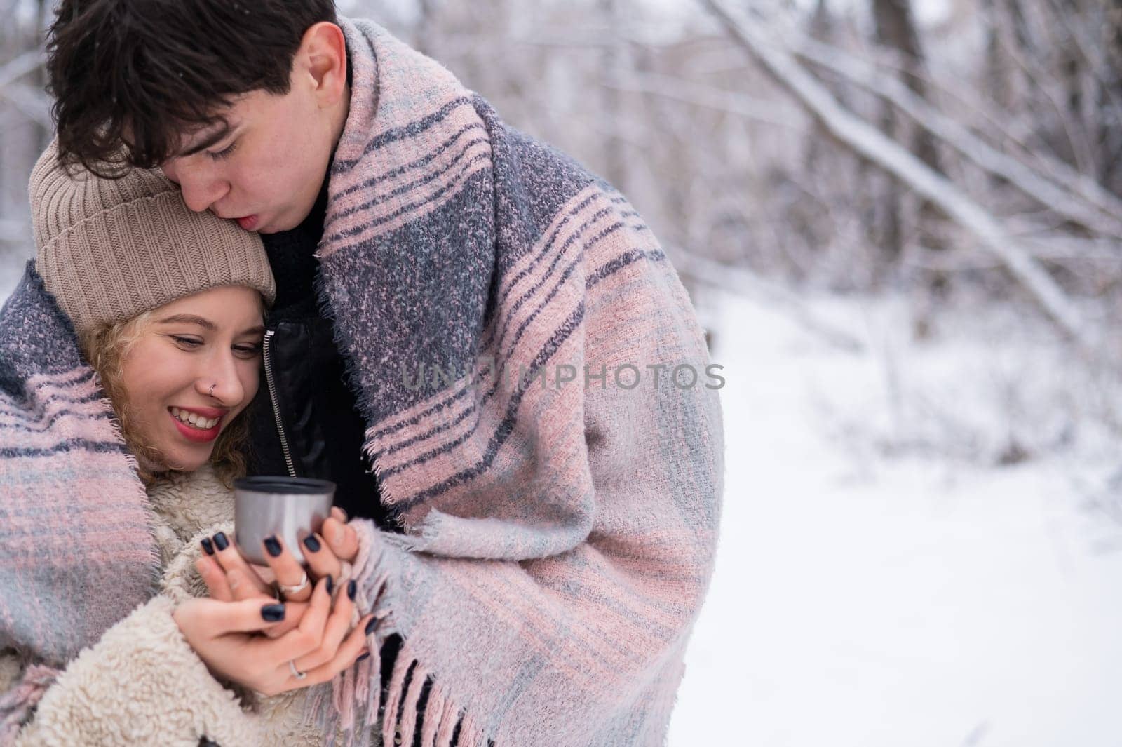 A young couple walks in the park in winter. The guy and the girl are drinking a warming drink outdoors