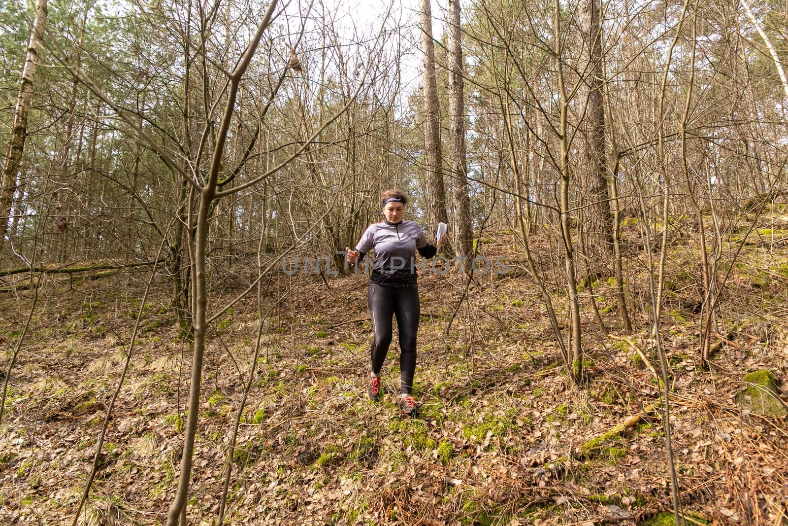 Grodno, Belarus - 25 March, 2023: Strong caucasian young woman wearing sportswear running through a forest during exercise in outdoor orienteering Grodno Forest Day. Belarus, hobby sport.