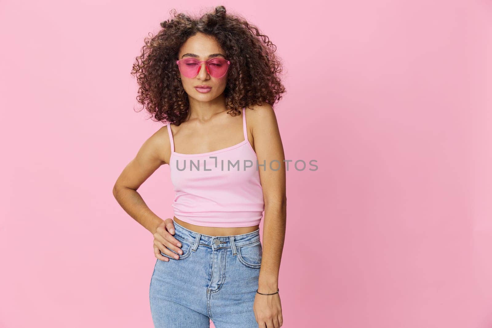 Happy woman afro curls hair dancing on pink background smile with teeth in summer pink t-shirt jeans and glasses, summer vibe, copy space. High quality photo