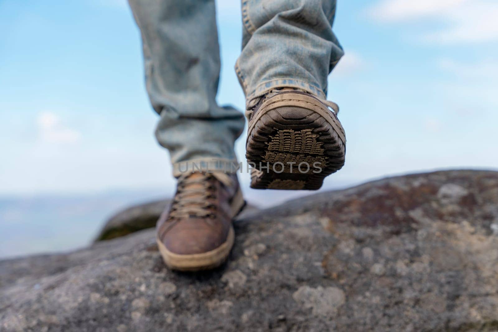 man in special boots walking in the mountains reaching the destination and on the top of mountain in Peak District against blue cloudy sky on sunny day Travel Lifestyle concept by Iryna_Melnyk