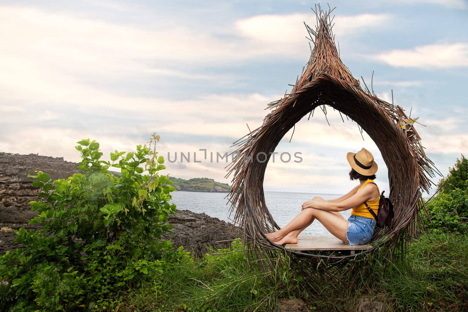Female traveler relaxing sitting in straw nest looking at ocean view. Woman contemplating sea landscape. Copy space. by Hoverstock