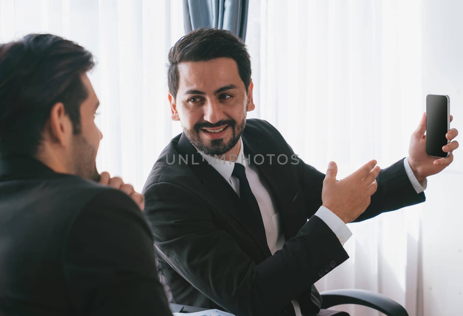 Business people wearing black formal suit in meeting office discussing on business matters and using smartphone. Professional businessman with happy look talking to coworker or client on desk. Fervent