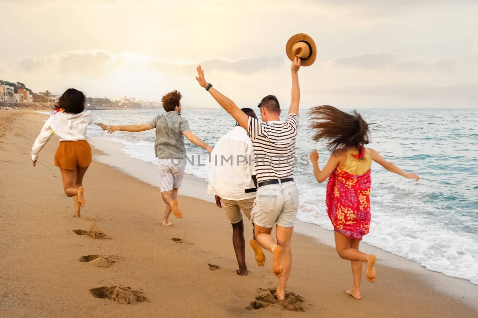 Rear view of happy multiracial group of young friends running on the beach during vacation summer. Copy space. Holiday concept.