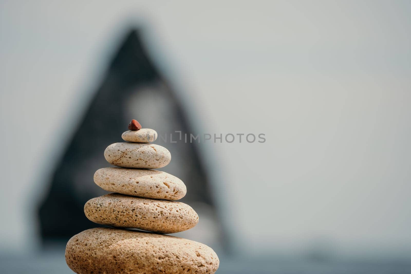 Pyramid stones on the seashore with warm sunset on the sea background. Happy holidays. Pebble beach, calm sea, travel destination. Concept of happy vacation on the sea, meditation, spa, calmness by panophotograph