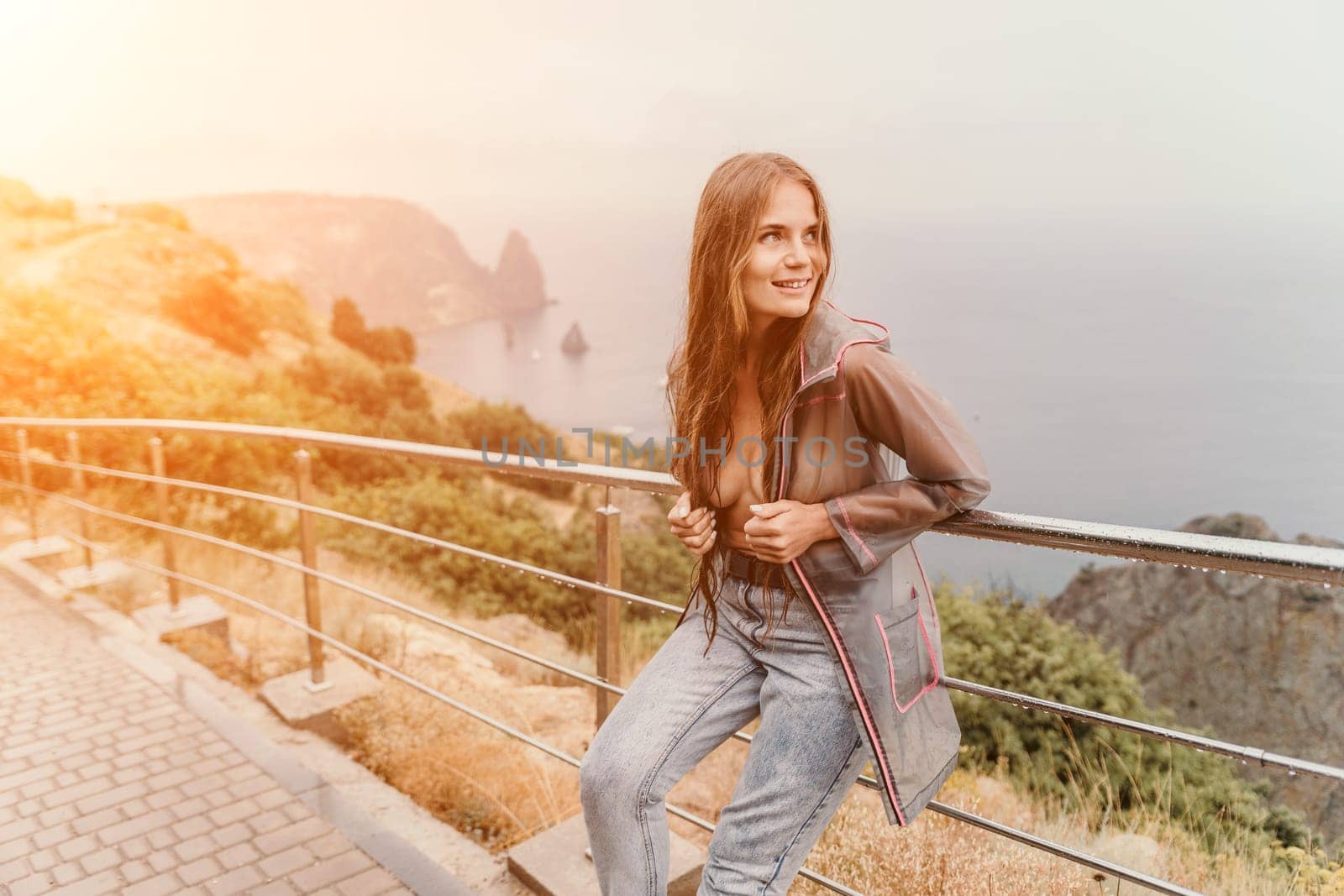 Woman rain umbrella. Happy woman portrait wearing a raincoat with transparent umbrella outdoors on rainy day in park near sea. Girl on the nature on rainy overcast day. by panophotograph