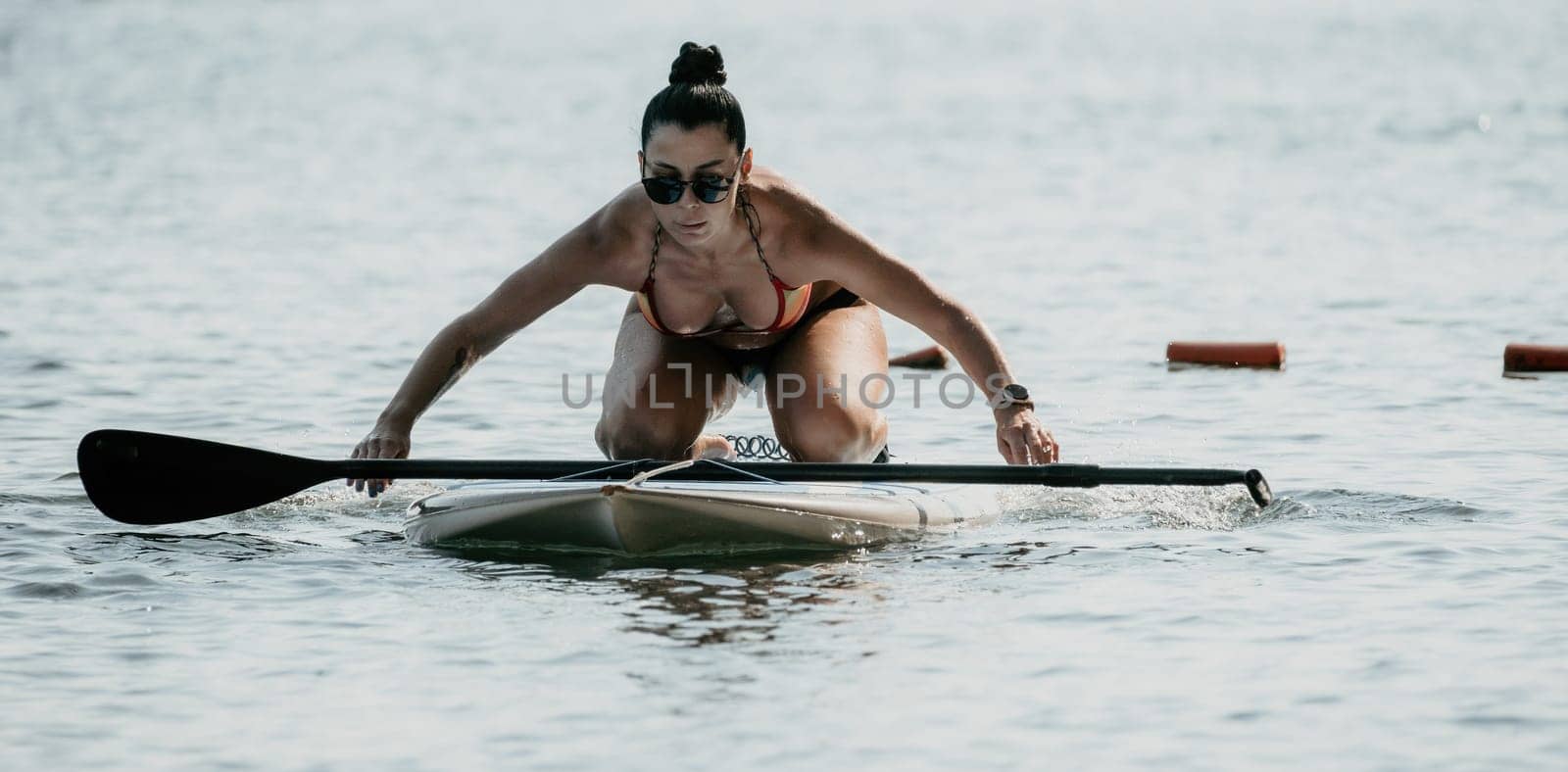 Sea woman sup. Silhouette of happy middle aged woman in rainbow bikini, surfing on SUP board, confident paddling through water surface. Idyllic sunset. Active lifestyle at sea or river