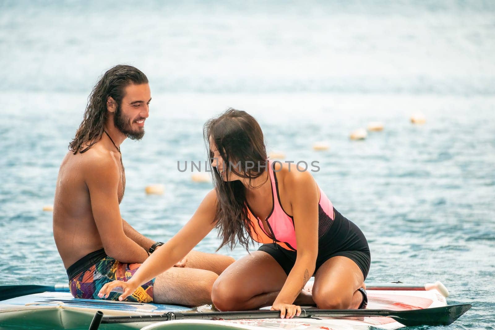 Sea woman and man on sup. Silhouette of happy young woman and man, surfing on SUP board, confident paddling through water surface. Idyllic sunset. Active lifestyle at sea or river