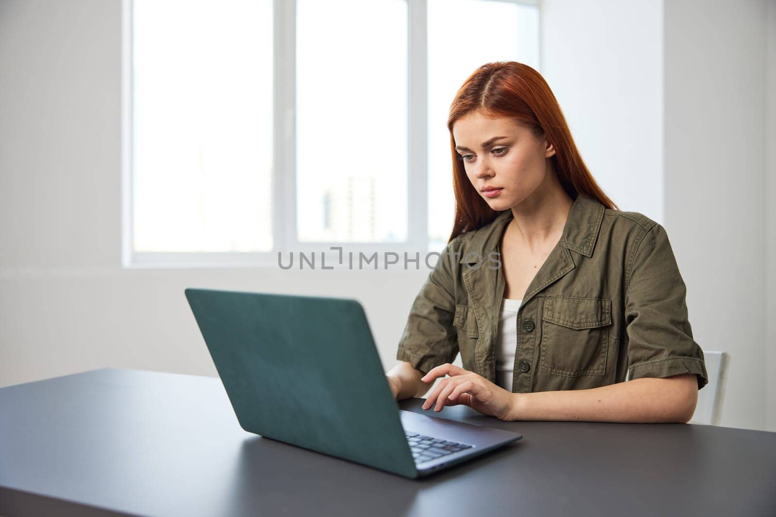 portrait of a red-haired woman in the office sitting thoughtfully at a laptop. High quality photo