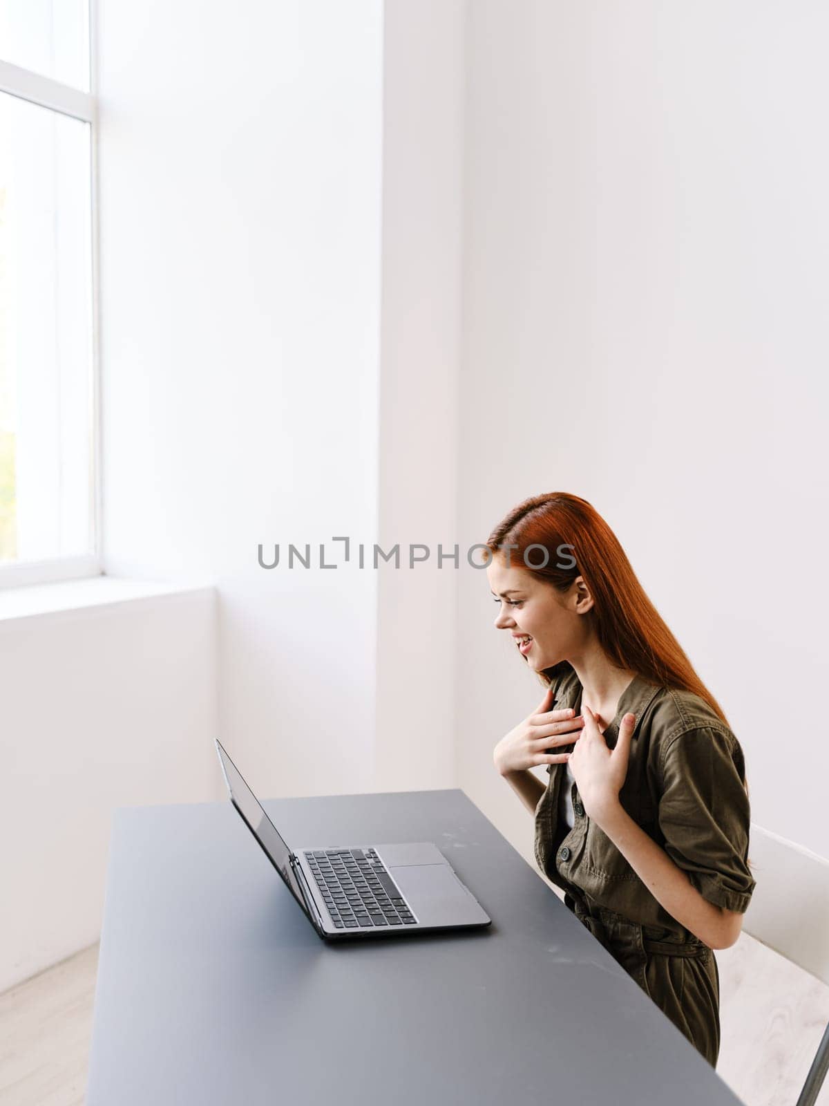 a slender, red-haired woman works at a laptop in a bright office room. High quality photo