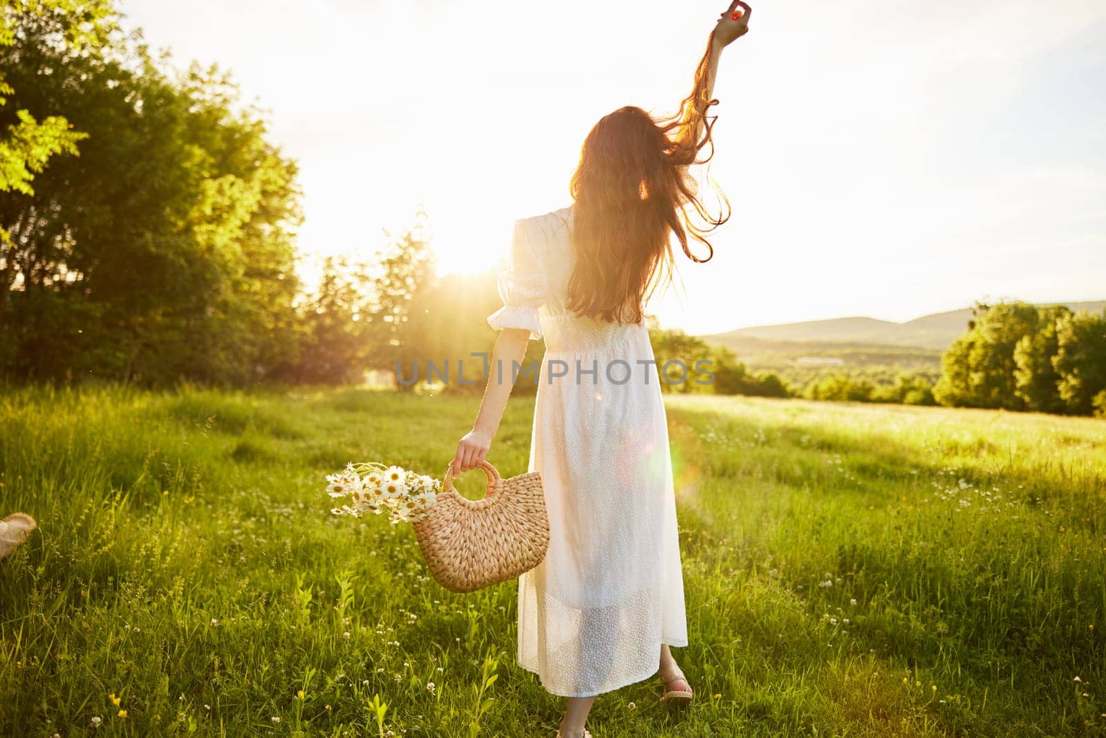 a girl in a long light dress stands in a field during sunset with her back to the camera. Full length photo. High quality photo