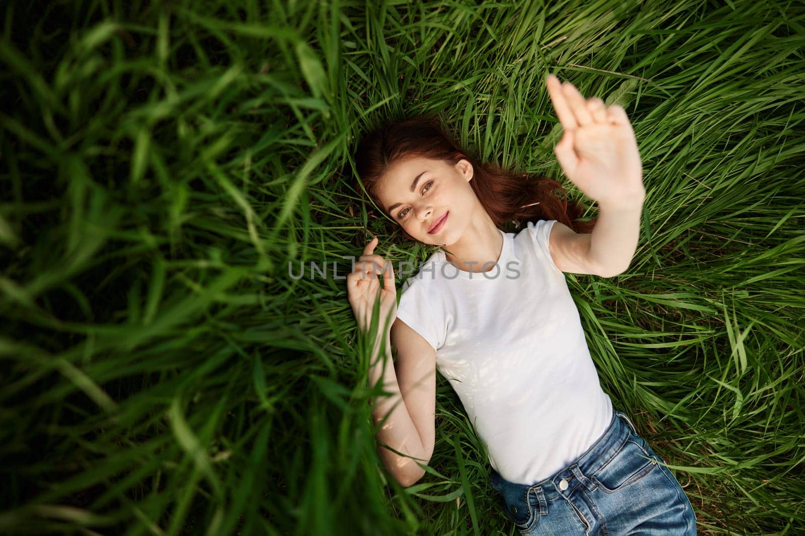 attractive teenager lying down on green grass with hands rised up to the air. High quality photo