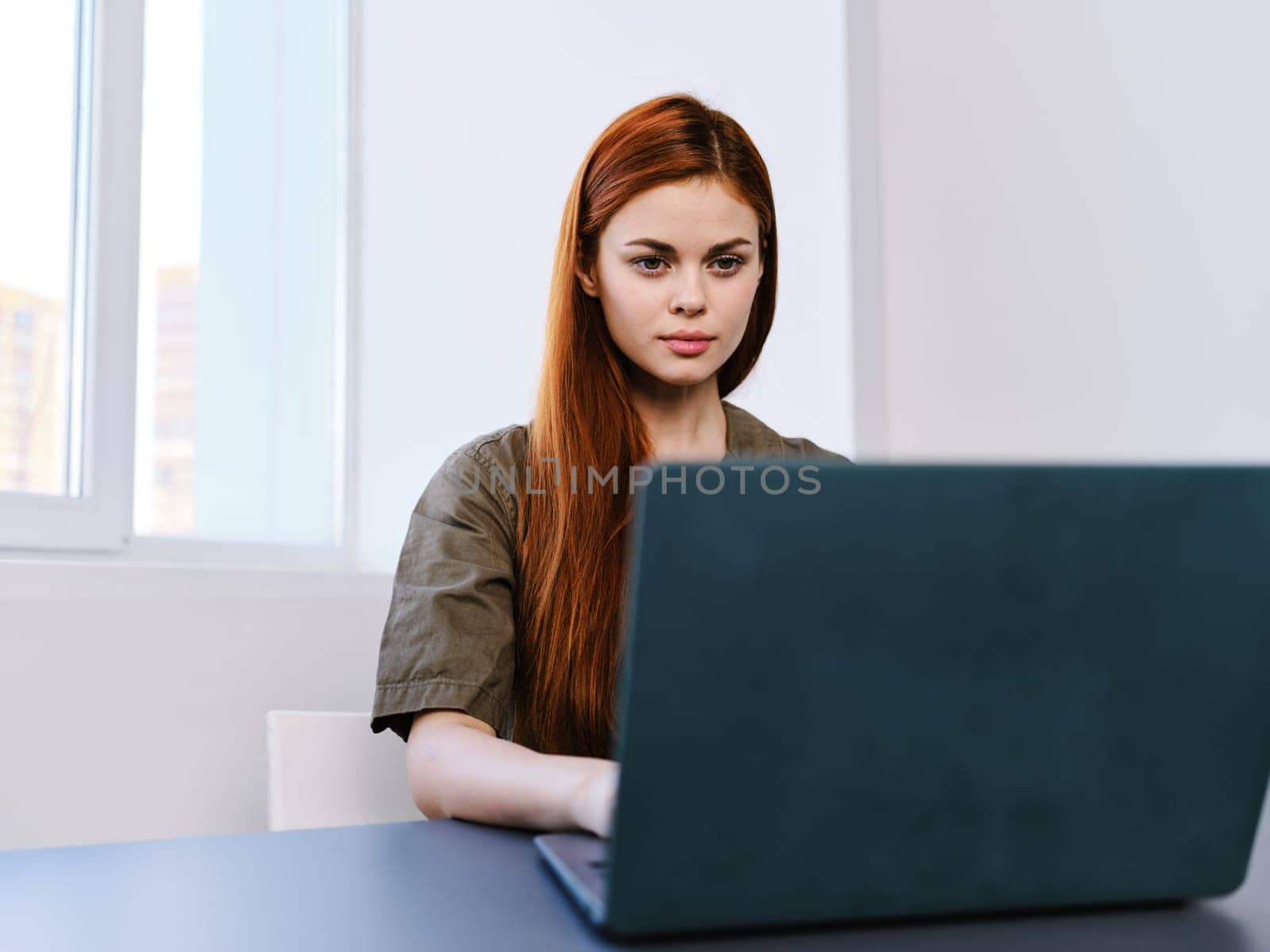 serious, puzzled woman sitting with a laptop at a table in a bright office. High quality photo