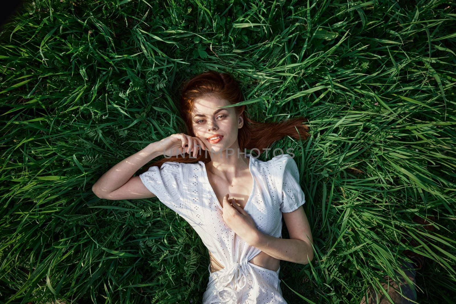 an elegant woman in a light dress lies in the grass and enjoys life by Vichizh