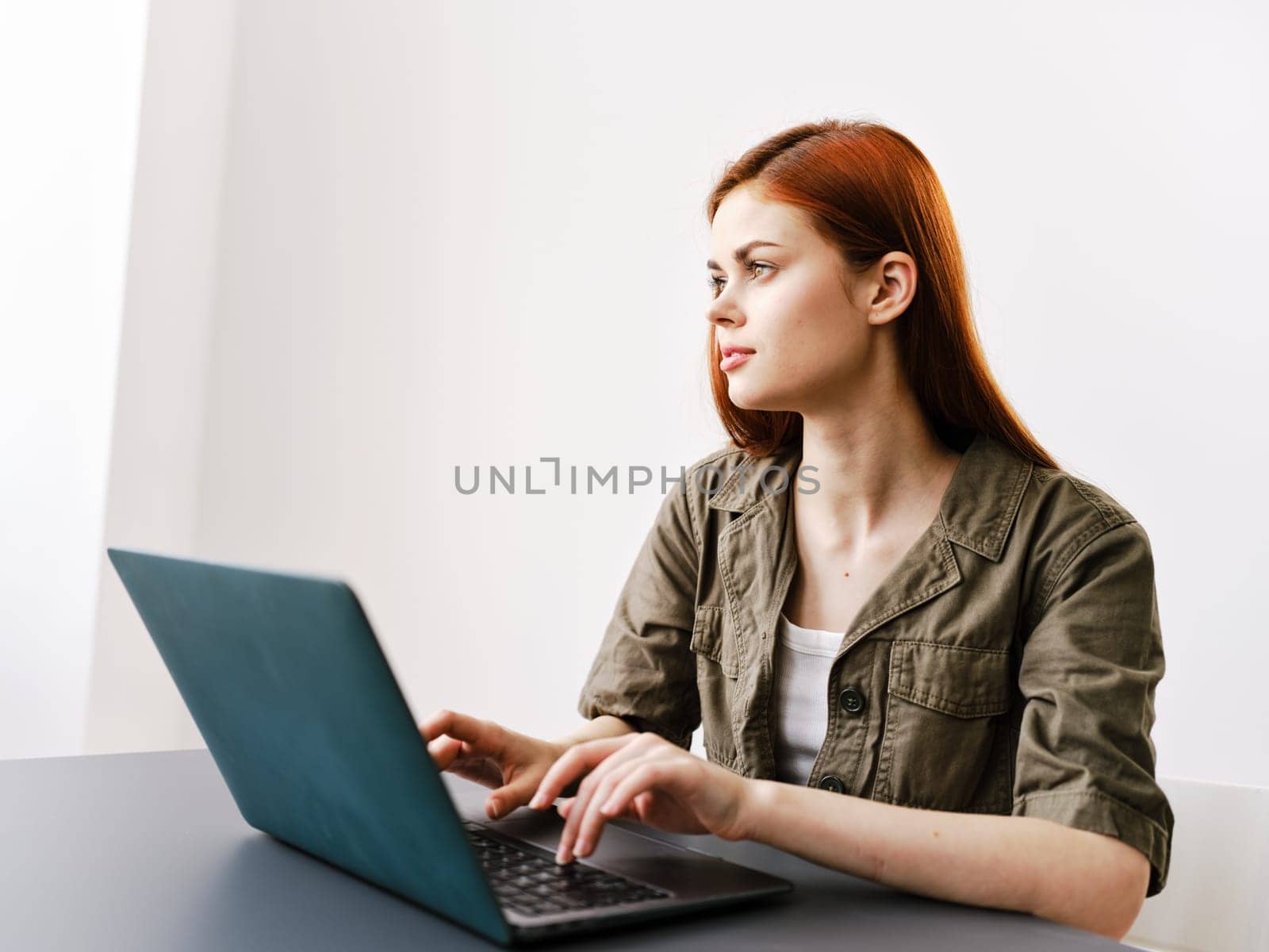 pensive redhead woman sitting at laptop while working in office by Vichizh