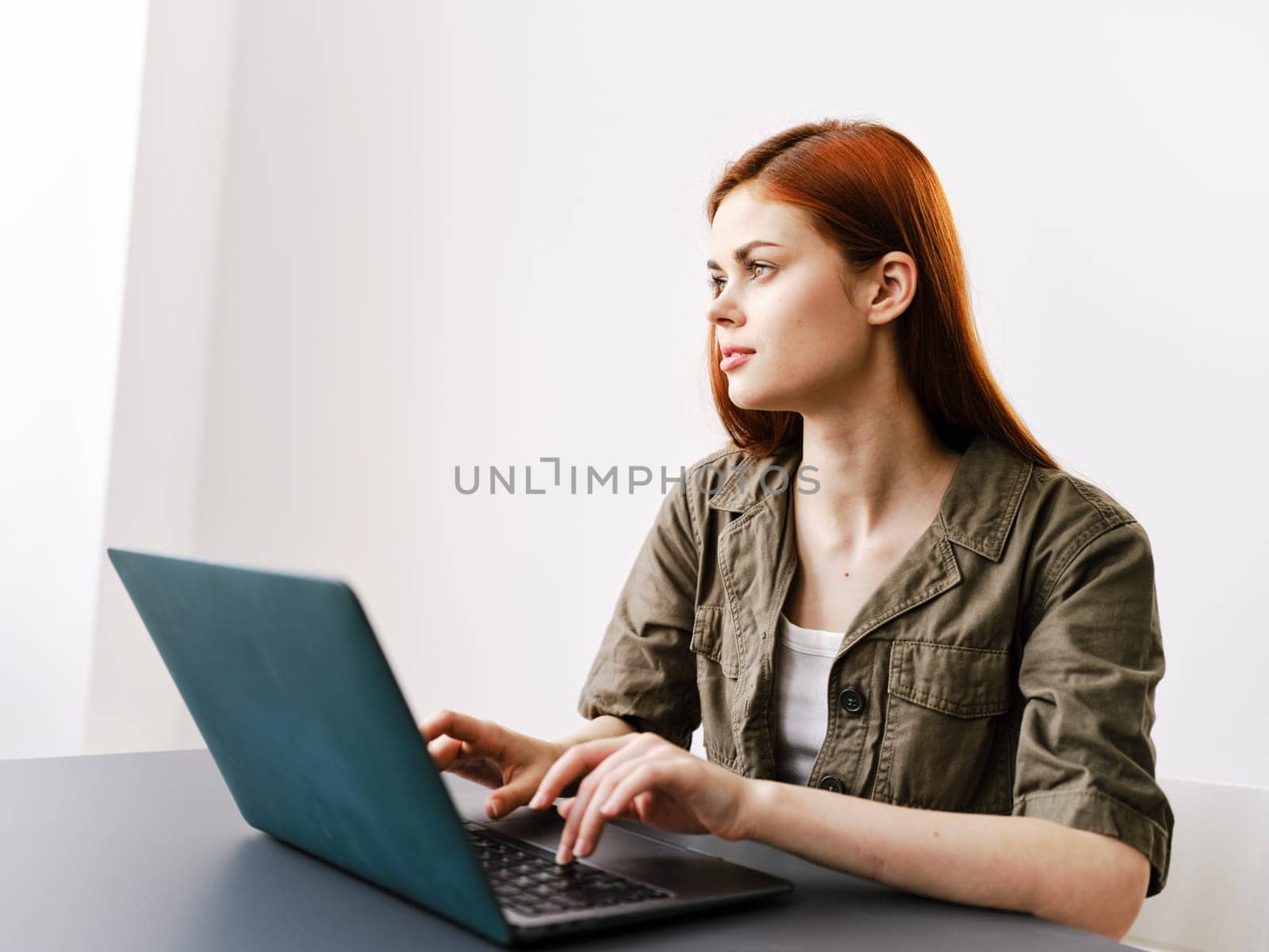 pensive redhead woman sitting at laptop while working in office. High quality photo