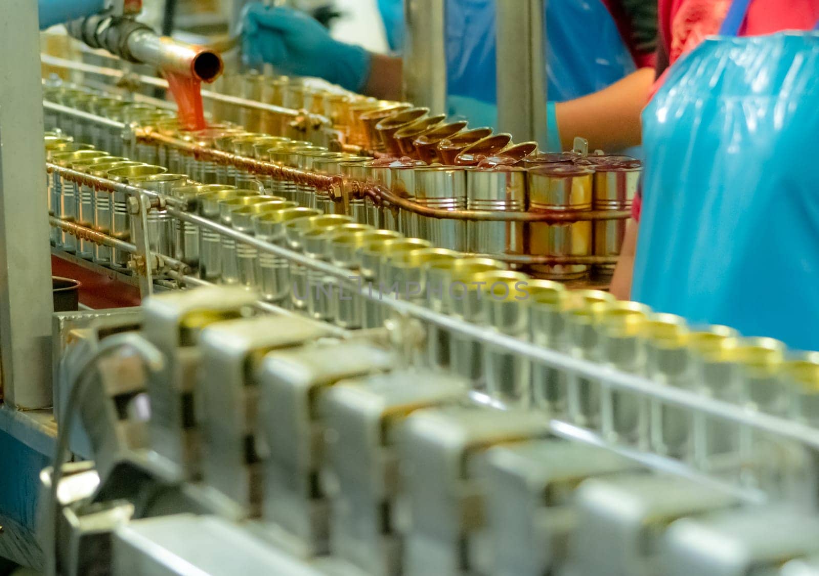 Canned fish factory. Food industry.  Sardines in red tomato sauce in tinned cans on conveyor belt at food factory. Blur workers working in food processing production line. Food manufacturing industry. by Fahroni