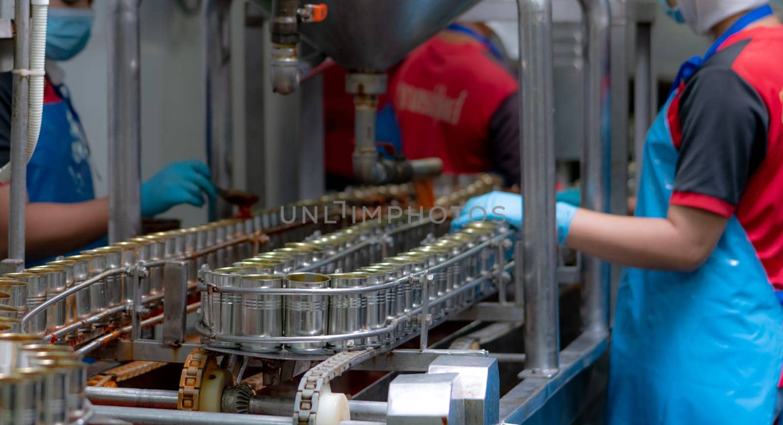 Canned fish factory. Food industry.  Sardines in red tomato sauce in tinned cans on conveyor belt at food factory. Blur workers working in food processing production line. Food manufacturing industry. by Fahroni