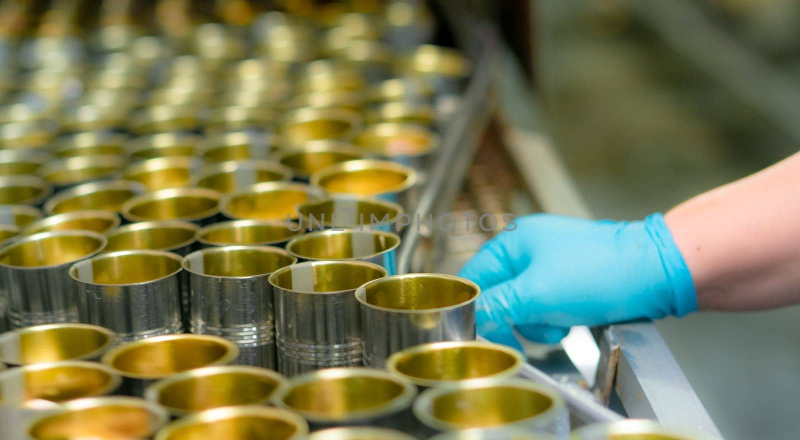 Selective focus on canned fish factory. Food industry. Food processing production line. Food manufacturing industry. Many can of sardines on a conveyor belt. Worker working in food processing factory. by Fahroni