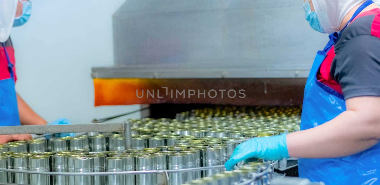 Canned fish factory. Food industry.  Food processing production line. Food manufacturing industry. Many can of sardines on a conveyor belt. Workers working in food processing factory. Cans industry. by Fahroni