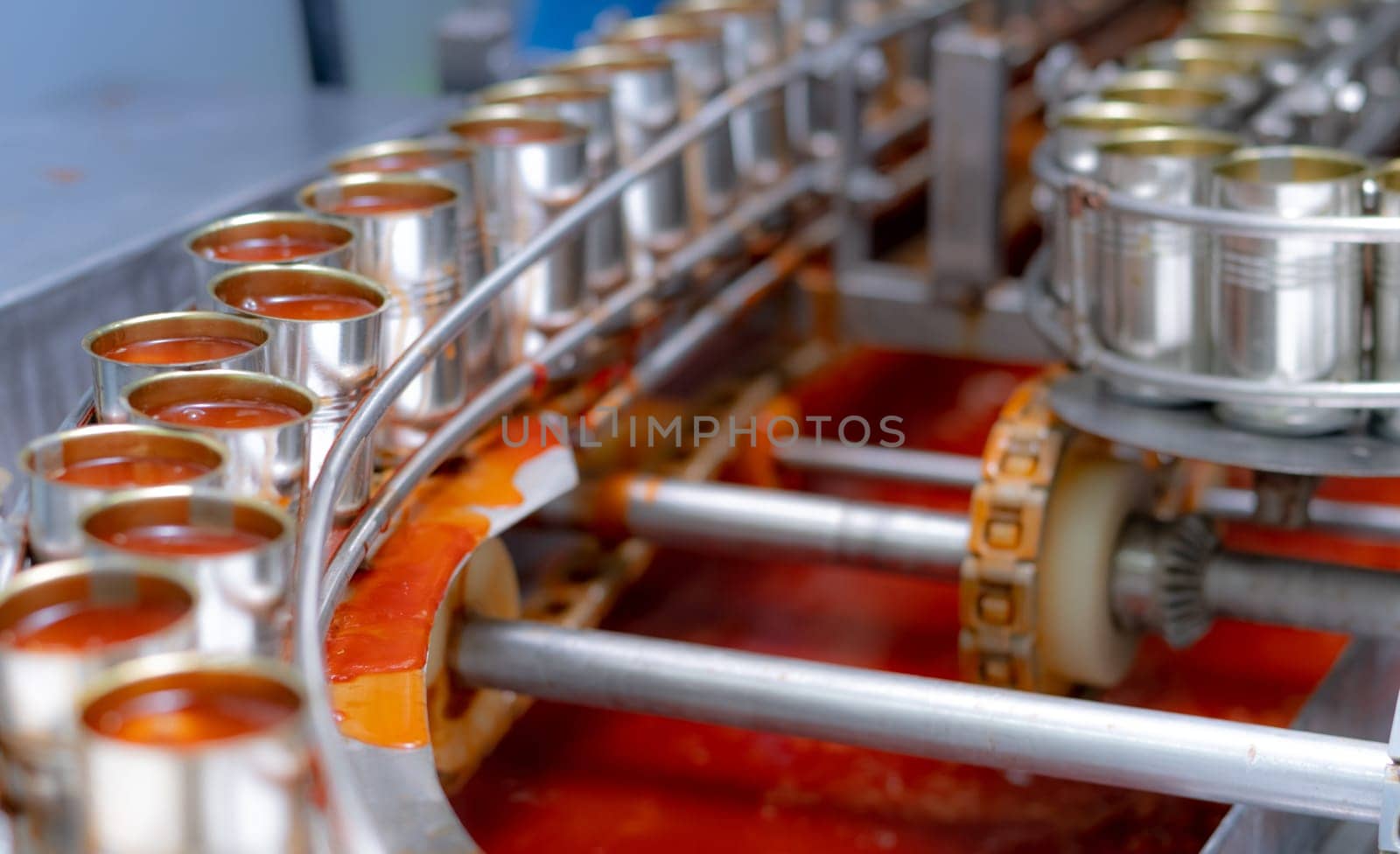 Canned fish factory. Food industry.  Sardines in red tomato sauce in tinned cans at food factory. Food processing production line. Food manufacturing industry. Many can of sardines on a conveyor belt. by Fahroni