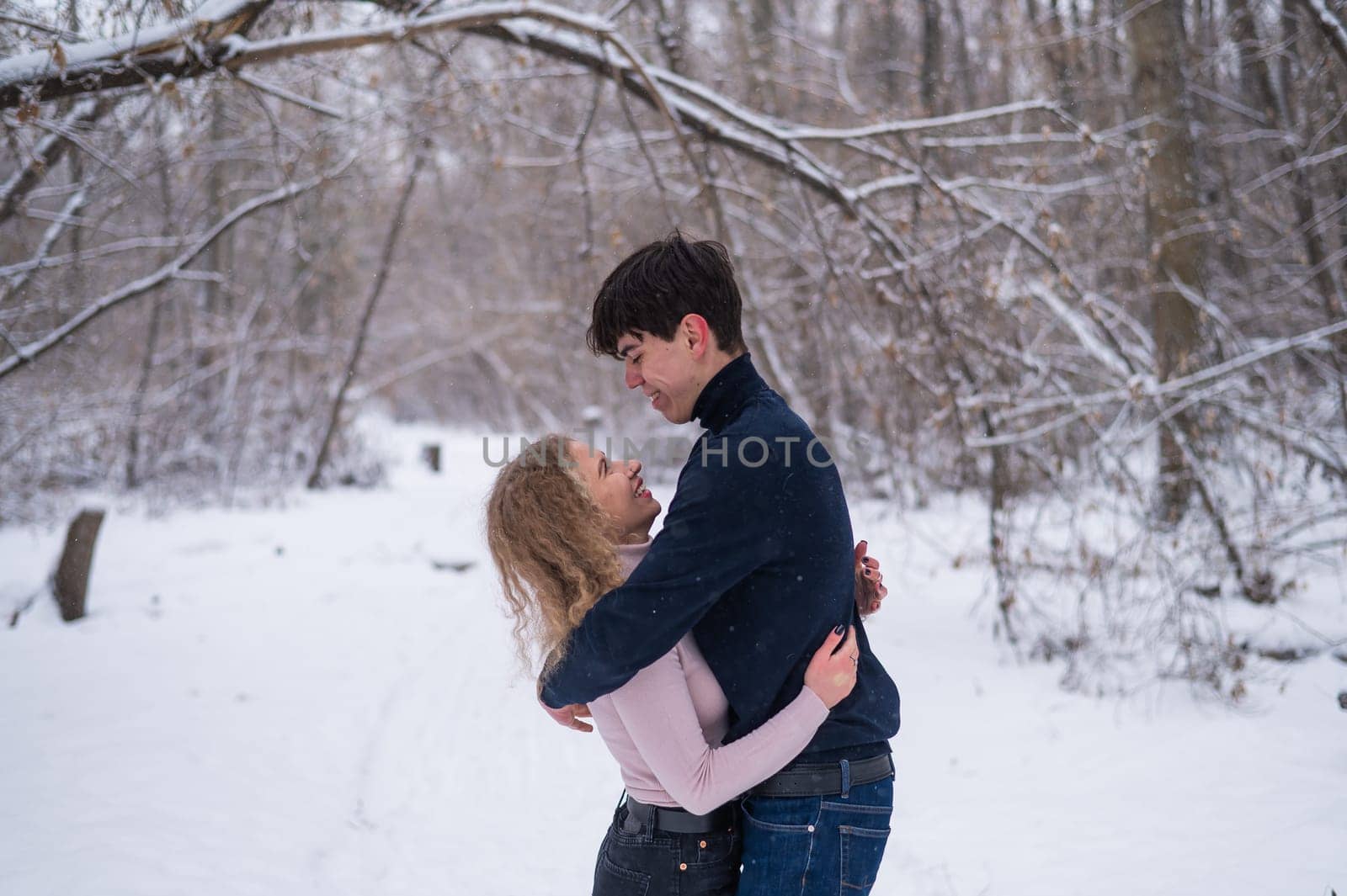 A young couple walks in the park in winter without jackets. Boy and girl hugging on the street