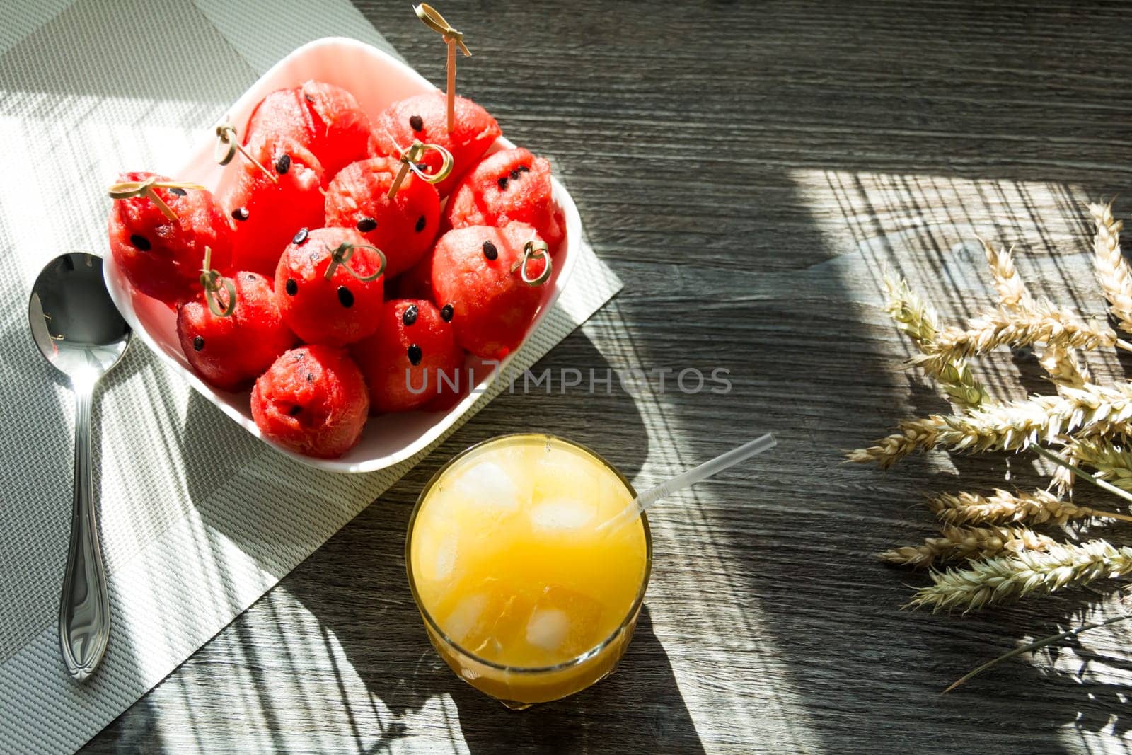 Freshly squeezed orange juice, sweet watermelon dessert and spikelets of ripe wheat on a wooden table in the sunlight... by Alla_Yurtayeva