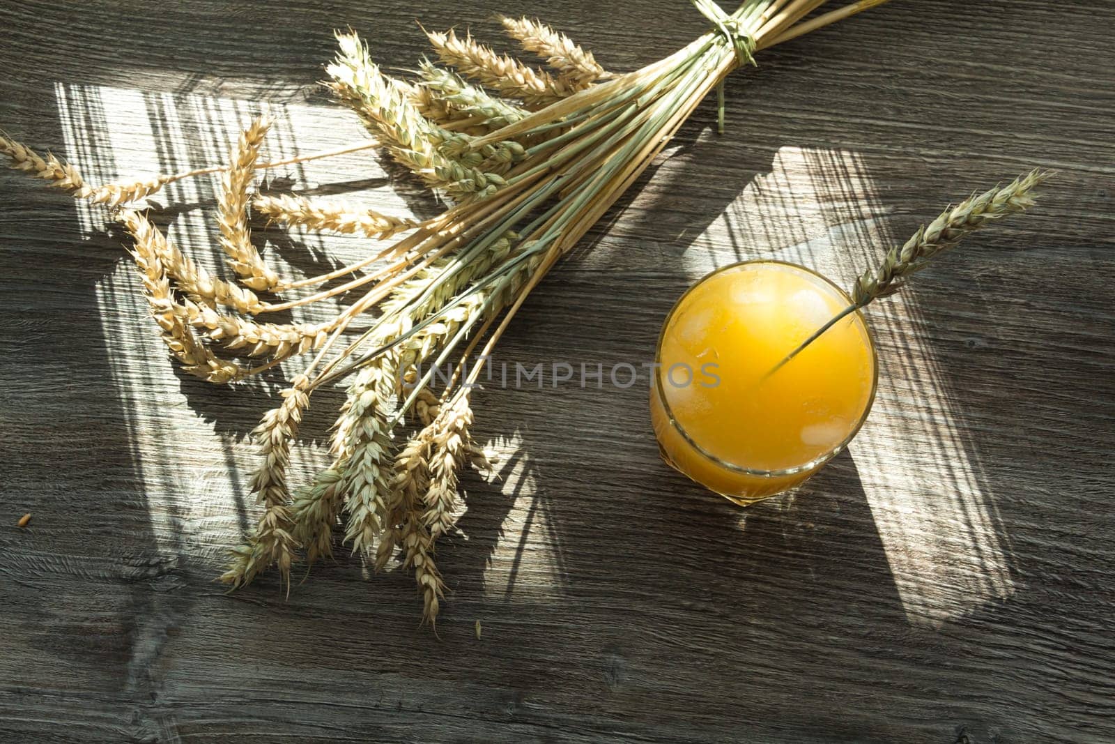 Freshly squeezed yellow juice and spikelets of ripe wheat on a wooden table in the sunlight. by Alla_Yurtayeva