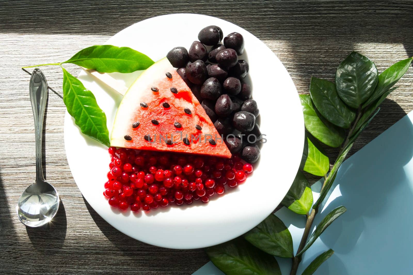 Summer snack. Fresh berries and fruits on a wooden table with green leaves of plants.