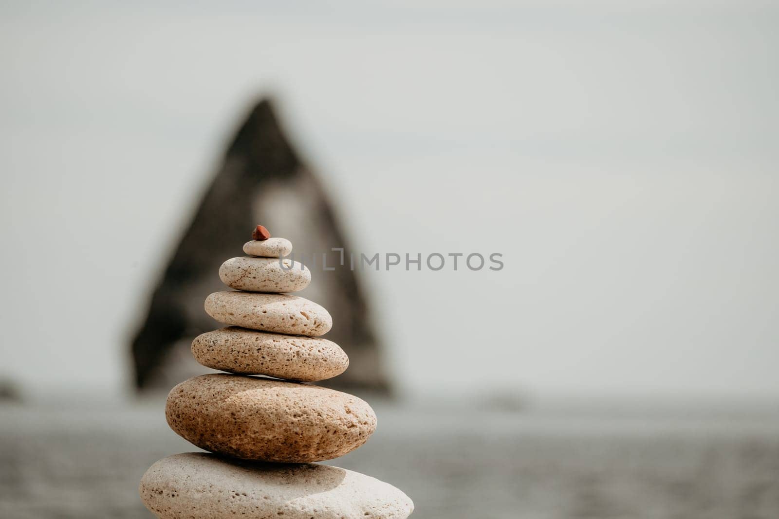 Pyramid stones on the seashore with warm sunset on the sea background. Happy holidays. Pebble beach, calm sea, travel destination. Concept of happy vacation on the sea, meditation, spa, calmness by panophotograph