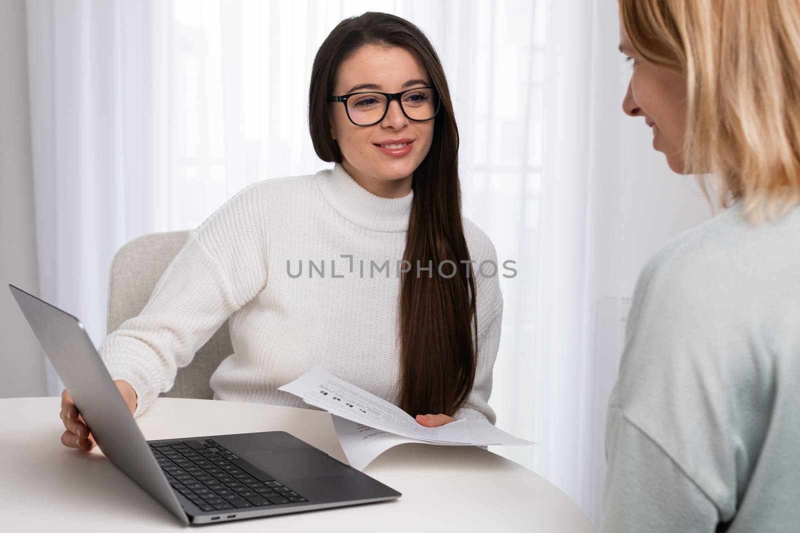 Female tutor explains material to lady student using Notebook and papers. Young woman in glasses conducts class teaching foreign languages