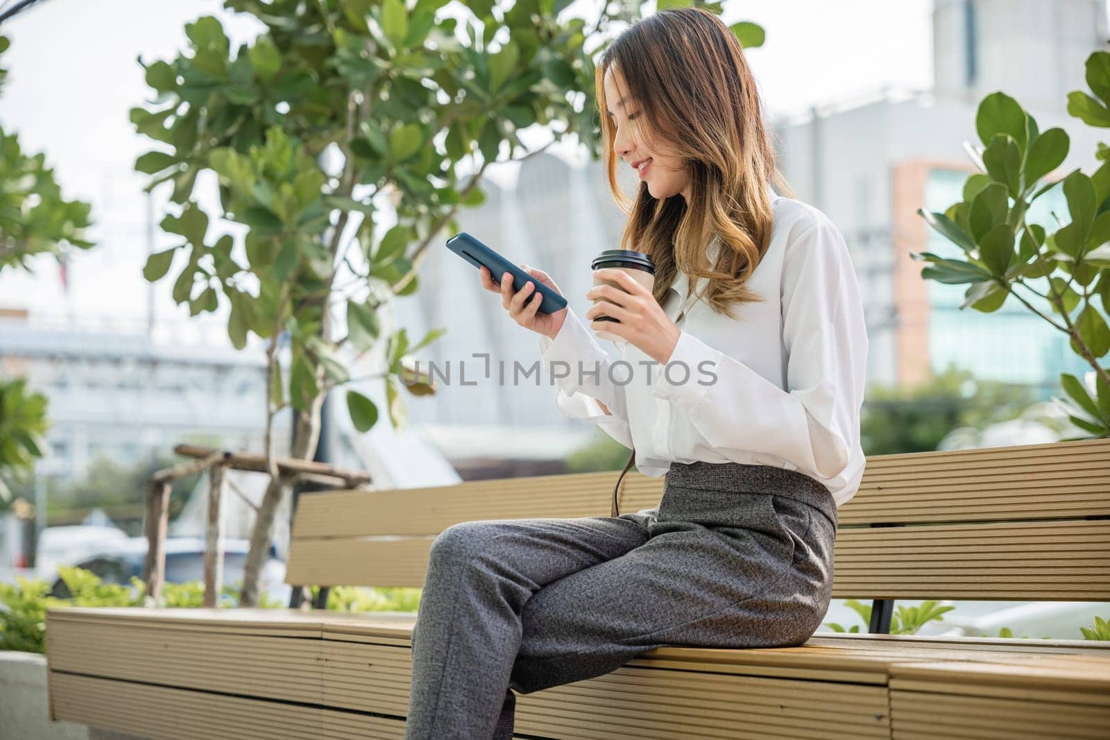 Smiling woman sitting on bench outdoor on the park using smartphone chatting social media by Sorapop
