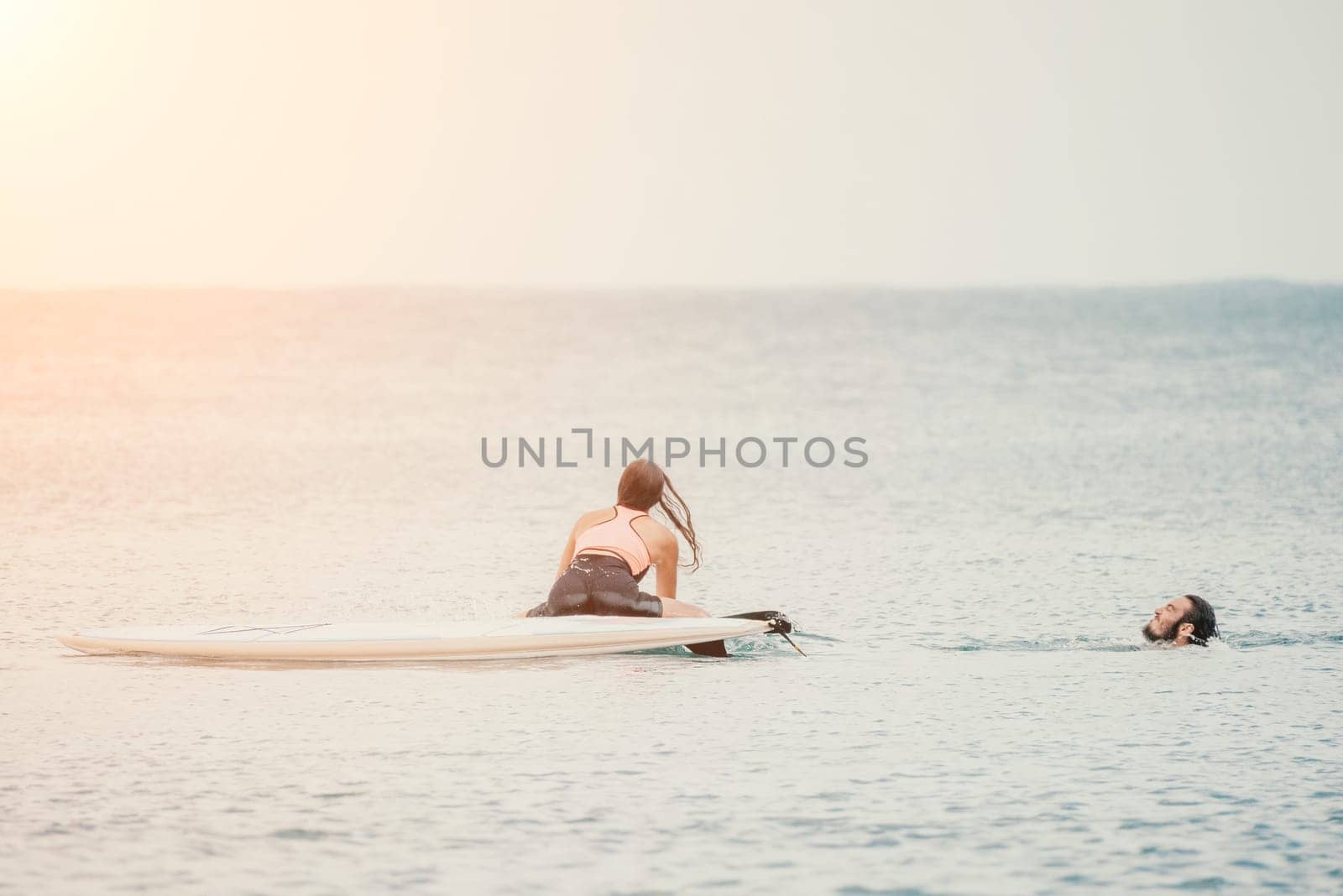 Sea woman and man on sup. Silhouette of happy young woman and man, surfing on SUP board, confident paddling through water surface. Idyllic sunset. Active lifestyle at sea or river