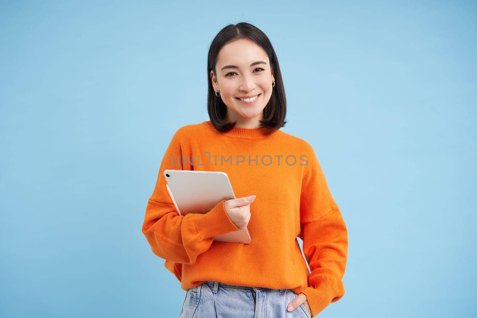 Smiling modern woman with tablet, looking confident, student with her gadget, standing over blue background.