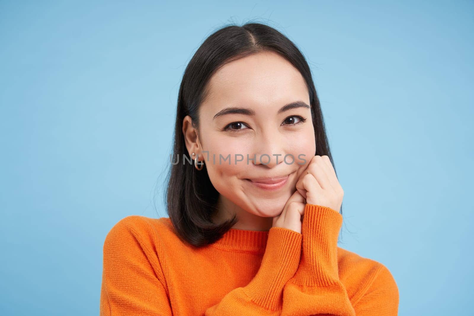 Close up of candid young female model laughs and smiles, shows natural happy emotions, stands over blue background.