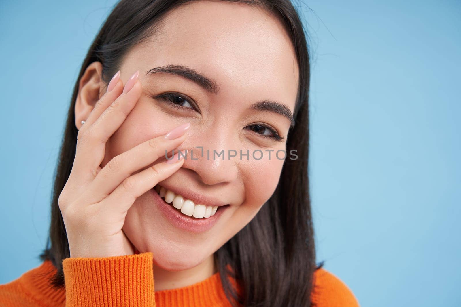 Beauty and skincare. Close up portrait of happy smiling japanese woman, touches her clear, glowing skin, natural healthy face, standing over blue background by Benzoix