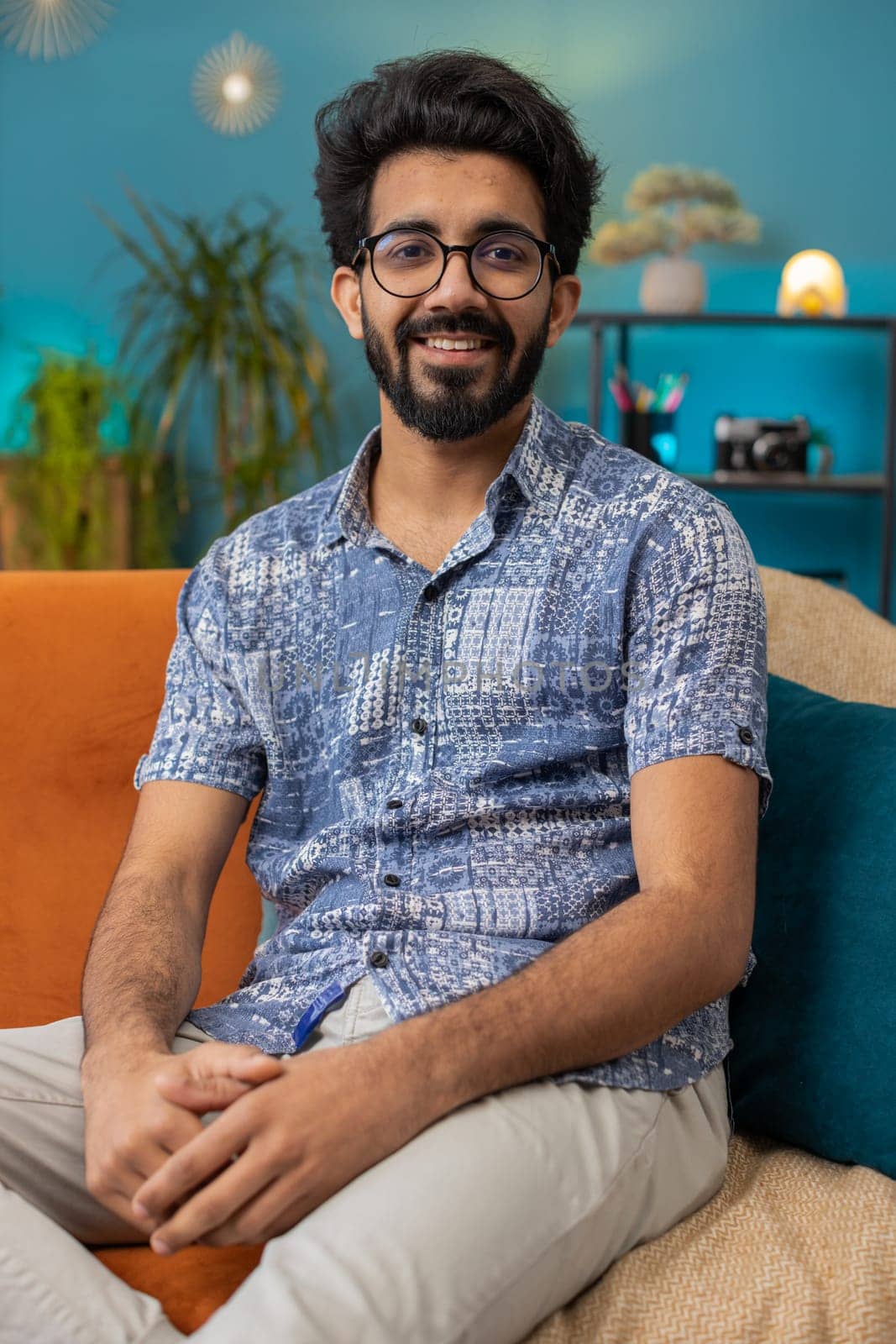 Portrait of happy calm indian man at home couch smiling friendly, glad expression looking away dreaming resting, relaxation feel satisfied concept good news, celebrate win. Hindu guy in living room