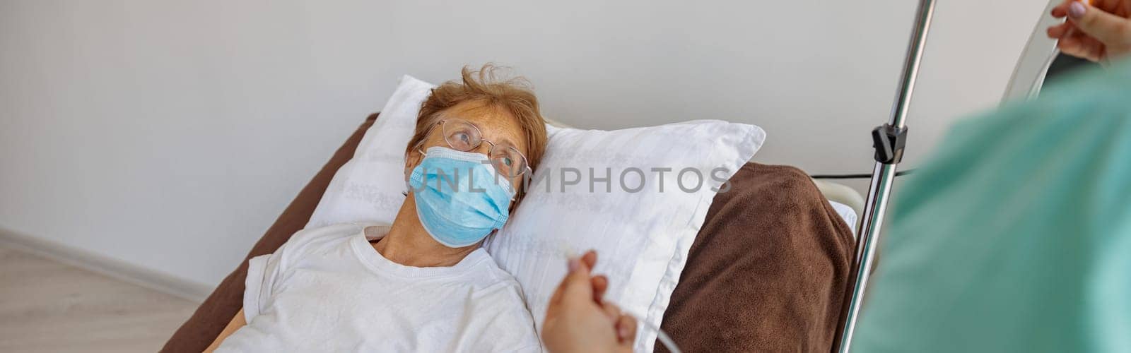 Nurse putting a drip on the arm of her patient in mask during pandemic of Covid 19 by Yaroslav_astakhov