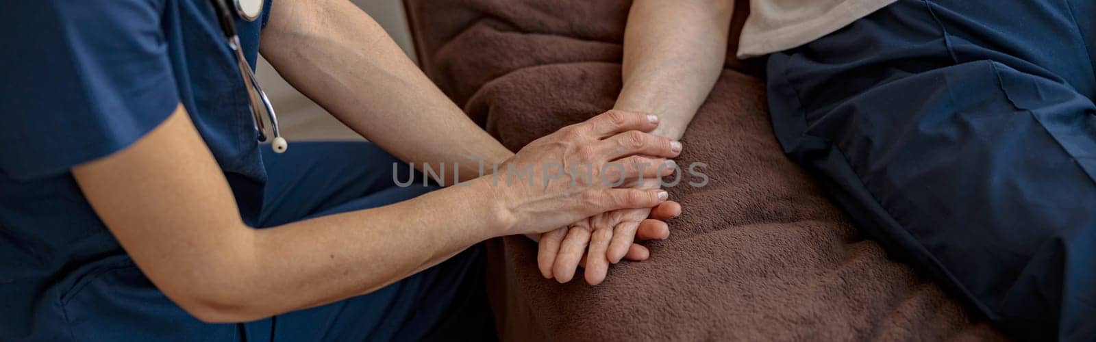 Doctor holding a sick senior patient by hand supporting her sitting in a hospital room