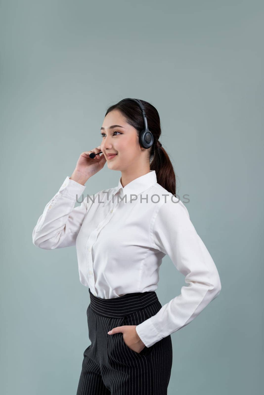 Attractive asian female call center operator with happy smile face advertises job opportunity on empty space, wearing a formal suit and headset on customizable isolated background. Enthusiastic