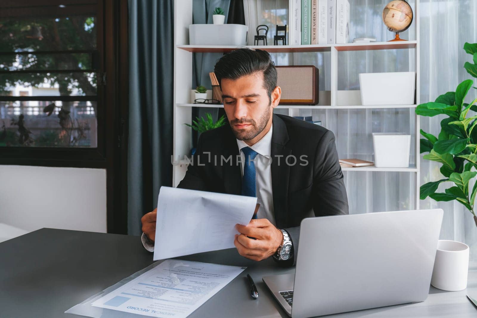 Modern professional businessman at modern office desk using laptop to work and write notes. Diligent office worker working on computer notebook in his office work space. fervent