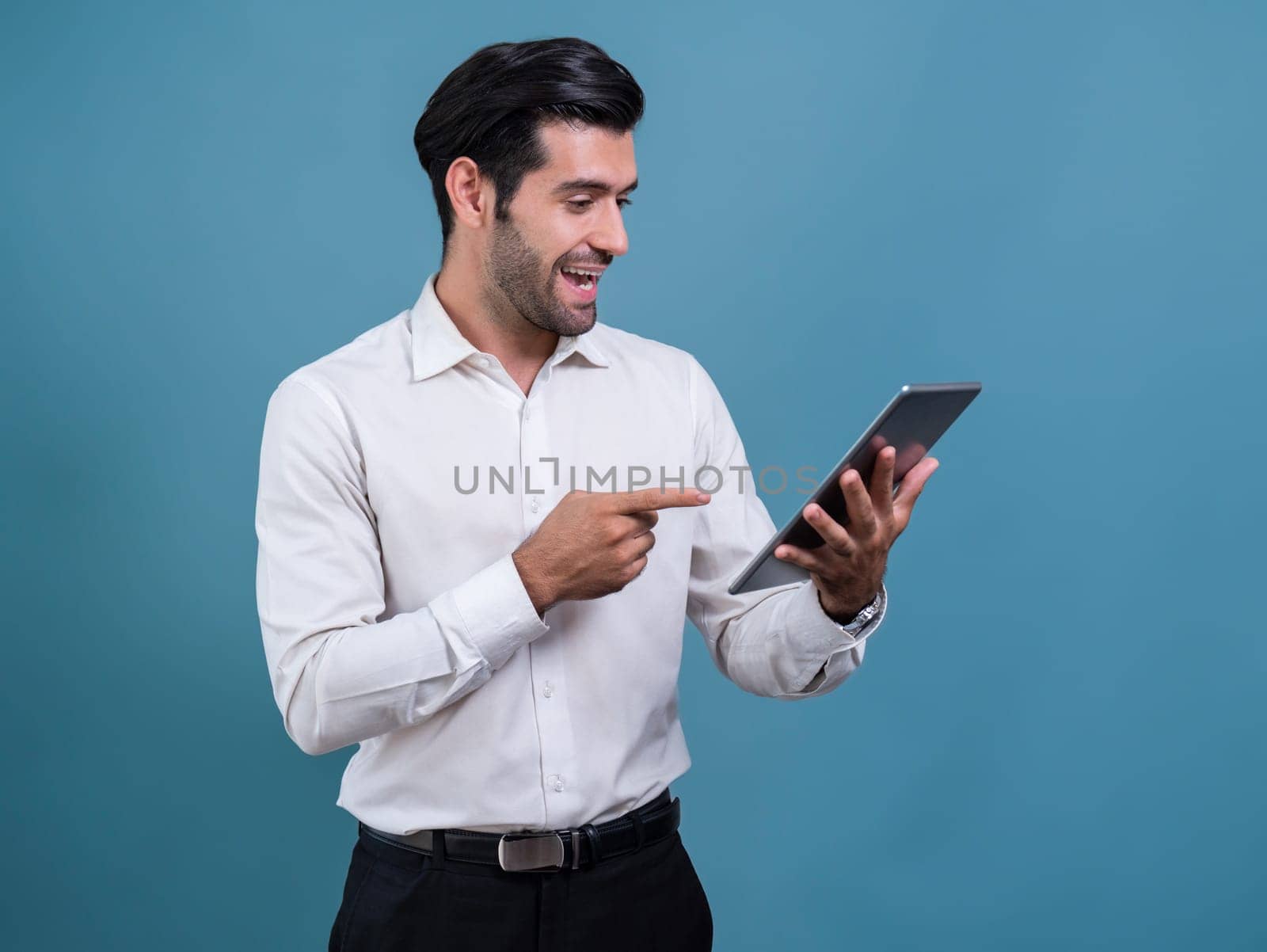 Confident businessman in formal suit holding tablet with surprise look for promotion or advertising. Facial expression and gestures indicate excitement and amazement on an isolated background. Fervent