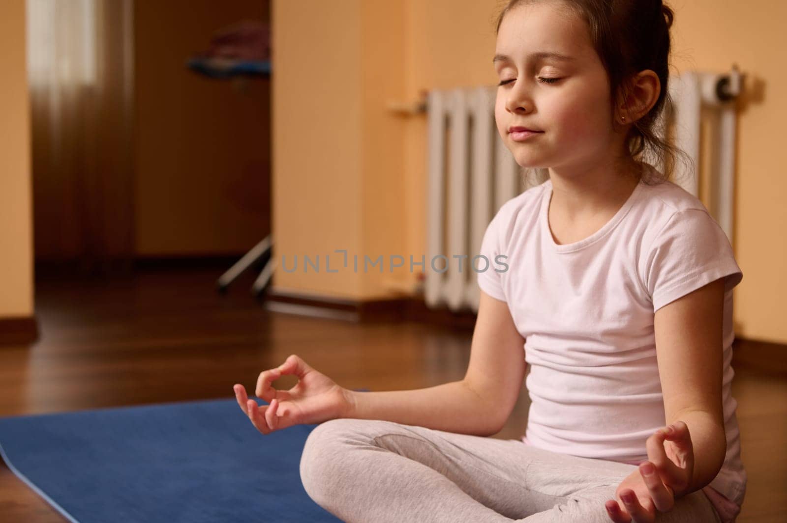 Portrait of a Caucasian peaceful cute little kid girl holding fingers in mudra gesture, meditating with her eyes closed. Little yogi feeling calm, positive and relaxed. Yoga practice and meditation