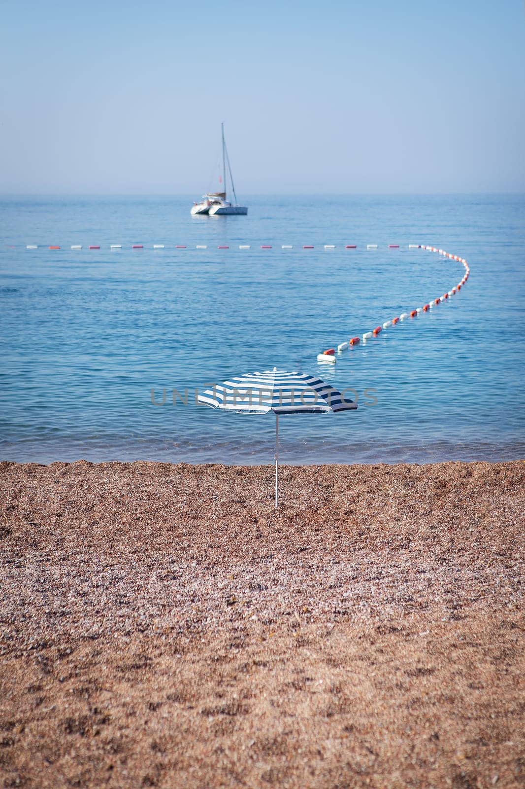 The famous resort island of St. Stephen in the Adriatic Sea, Montenegro. The concept of sea holidays, a yacht in the sea, a striped umbrella stands on a sandy beach