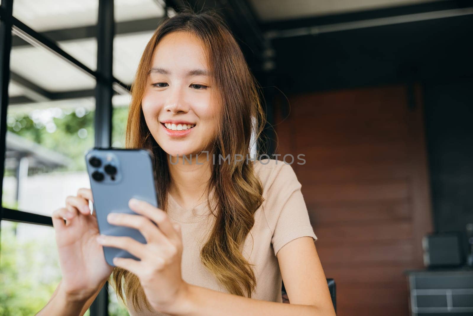 Beautiful Asian female hands holding and typing to communicate with others through on mobile phone, young woman using smartphone for shopping online at cafe coffee shop near windows in morning
