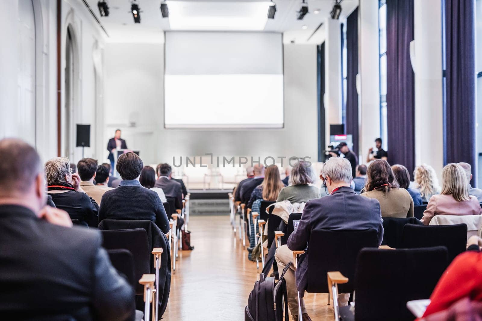 Speaker giving a talk in conference hall at business event. Rear view of unrecognizable people in audience at the conference hall. Business and entrepreneurship concept