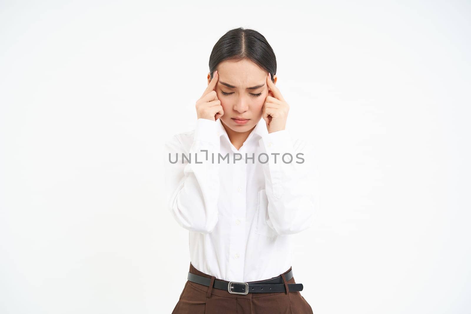 Image of asian serous looking woman, touches her head with upset face expression, has headache, suffers from migraine after stress at work, white background.
