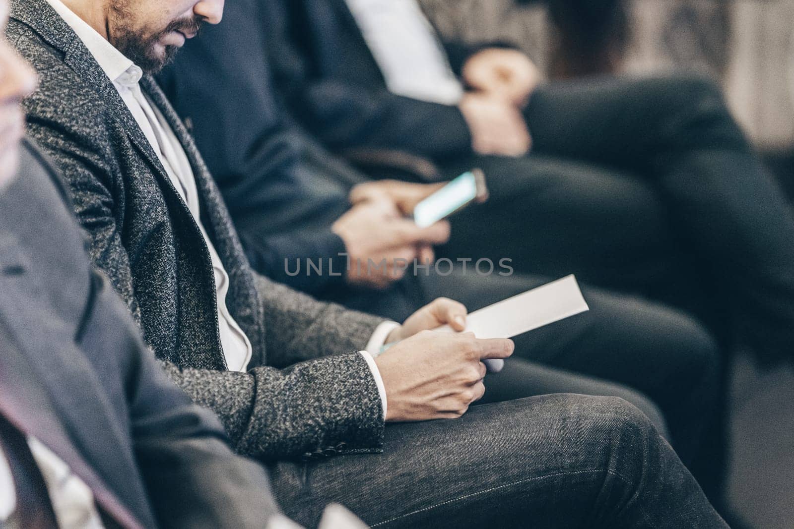 Businessman hands holding meeting brochure with program and schedules of business conference lectures. Event participants in conference hall