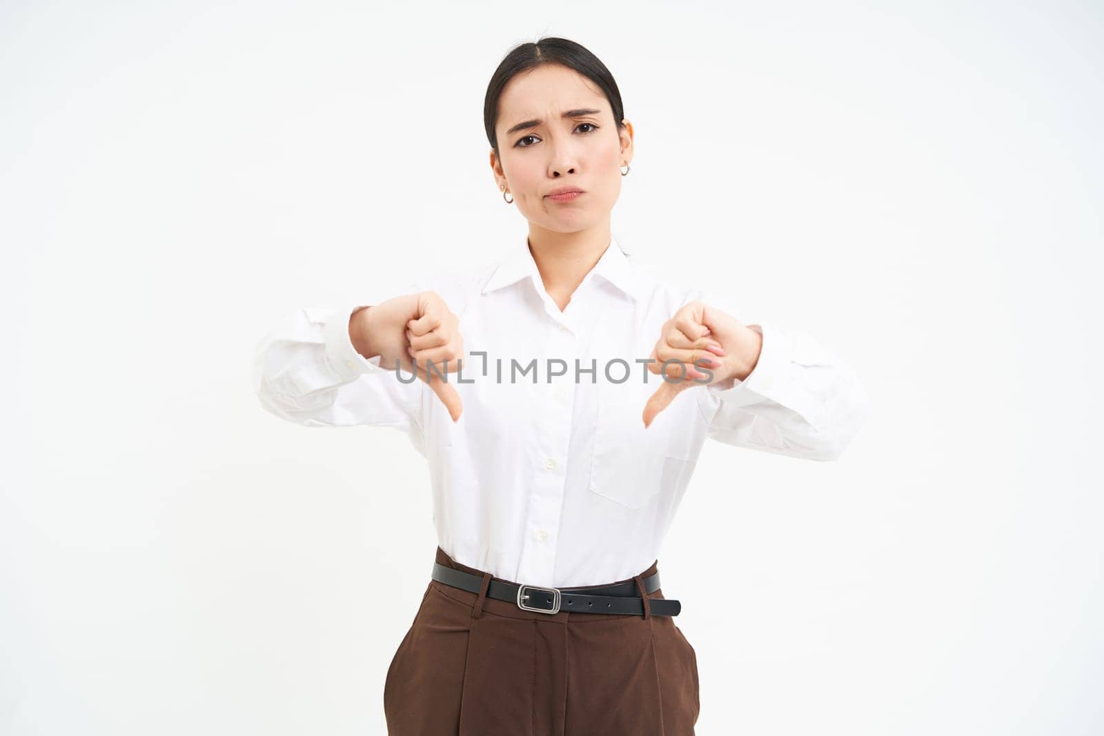 Image of disappointed woman, manager shows thumbs down and frowns with disapproval, white background.