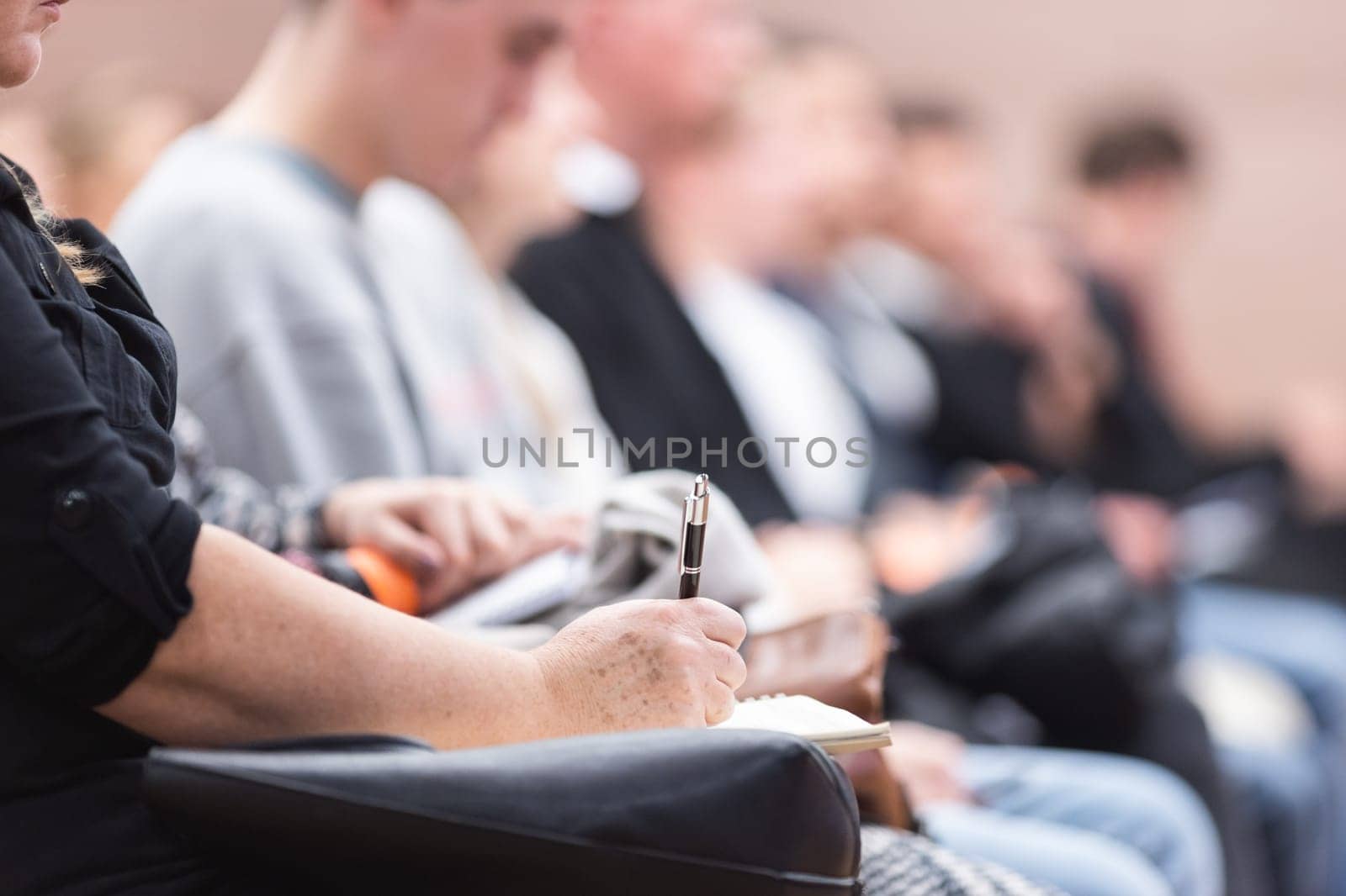 Female hands holding pen and notebook, making notes at conference lecture. Event participants in conference hall. by kasto